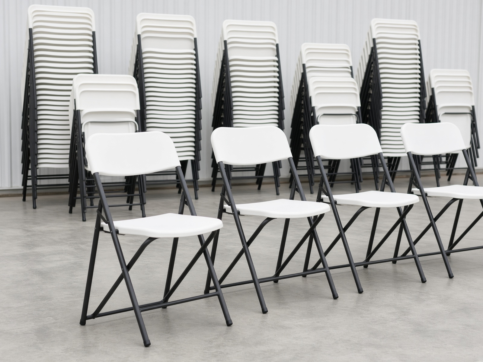 Stacks of newer white plastic folding chairs with black metal frames.